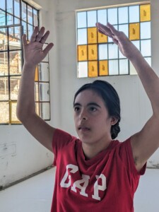 Girl doing a ballet move with her hands up in the air.